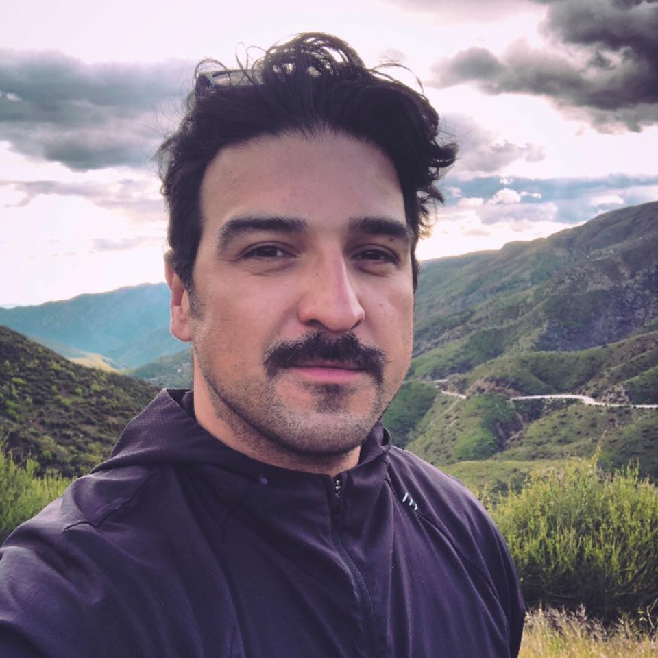 Man smiling at camera with trees and hills behind him
