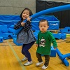 two young children play with foam tubes in an indoor gym