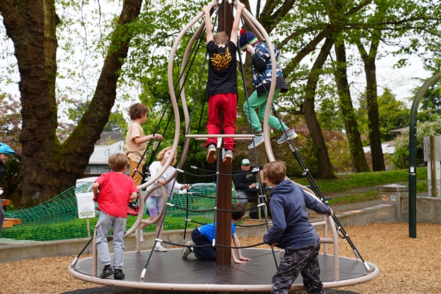 Children climb on a large circular rope spinner structure