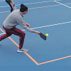 A player on a blue outdoor court hits a ball with a paddle.