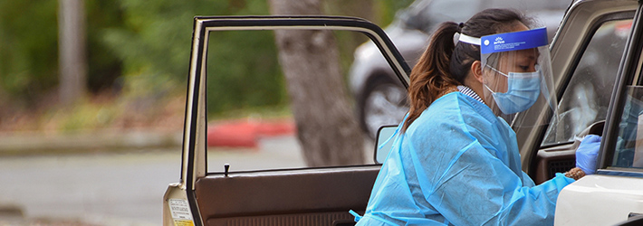 A nurse in personal protective equipment administering a COVID test at a drive-through site