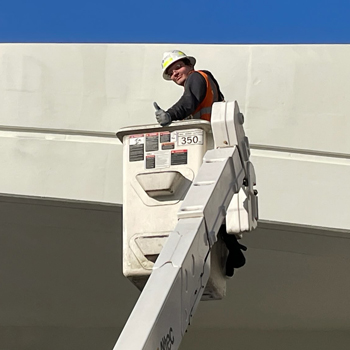 An SDOT employee performing bridge work in a crane, giving a thumbs up. 