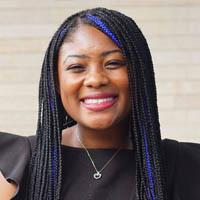 Naomi is smiling and has black braids and is wearing a black shirt