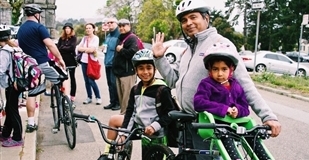 A smiling man and his two young children stand outside with their bikes
