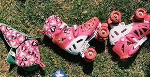 A set of pink roller skates lay on their sides in the grass on a sunny day