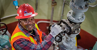 A smiling SPU employee in protective gear with hand on a pipe valve.
