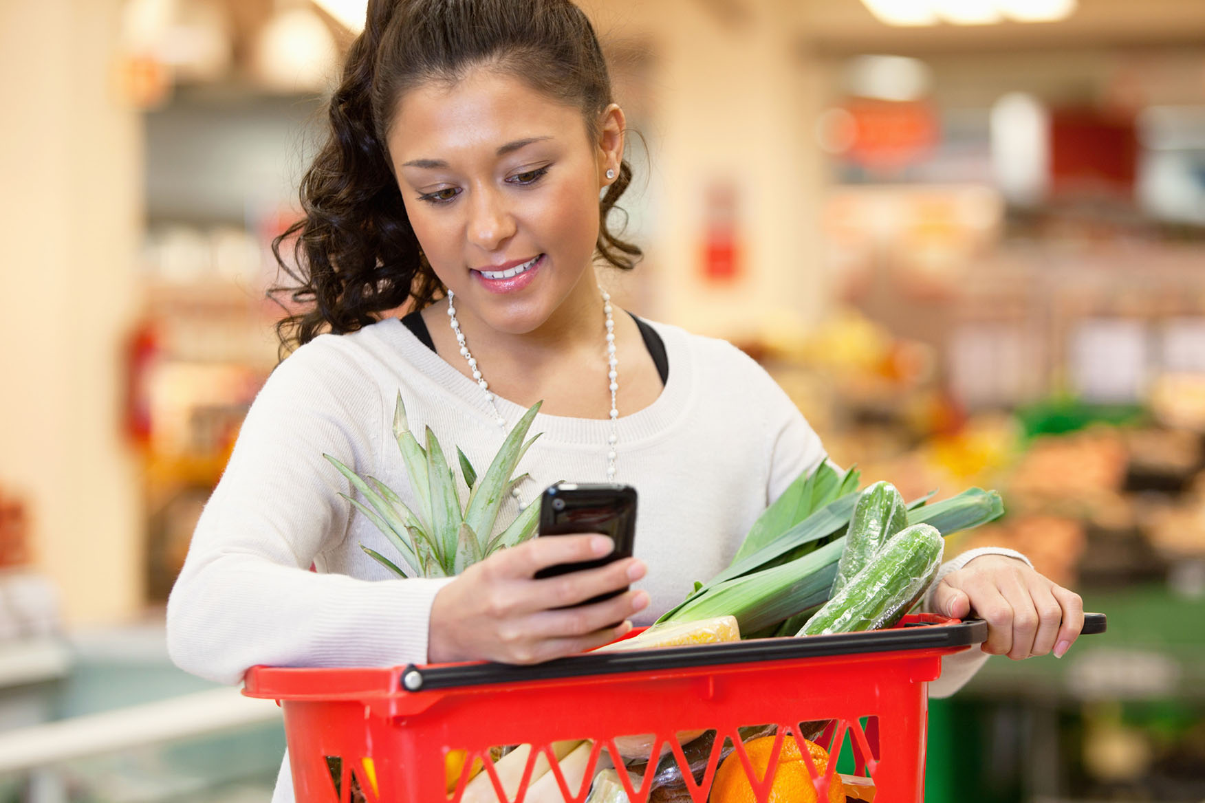 Woman checking shopping list on her phone while she holds a grocery basket.