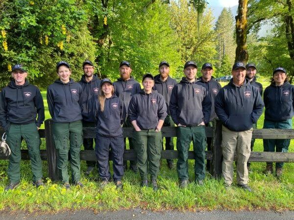 Fourteen members of the SPU Wildland Fire Crew, in matching black shirts and caps, pose for a group photo.