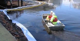 Two members of spill response team in a boat close to shore deploying spill containment equipment.