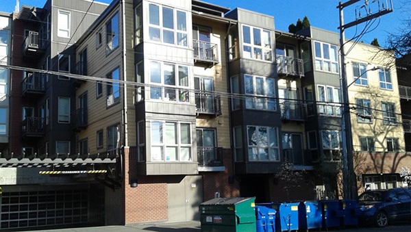 Photo of a typical multistory, multi-family housing property with collection dumpsters in front.