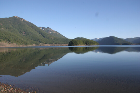 Photograph of a placid Chester Morse Lake with cloud-free blue sky above it.