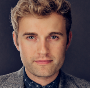 Headshot of person with fair skin, short curled blonde hair, smile, and in a button shirt with blazer.