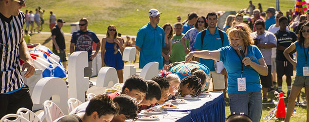 A judge stands over a food-eating event outdoors