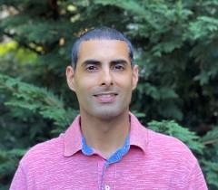 A man smiling wearing a pink shirt