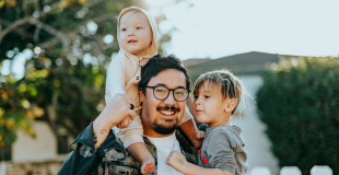 Man with small children smiling with a house in the background