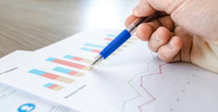 Hand holding a pen hovering over paperwork showing bar graphs