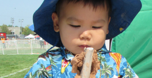 Child outside holding a stick with clay on it