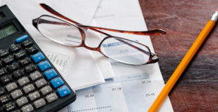 Calculator, pencil, glasses, and paperwork on a desk