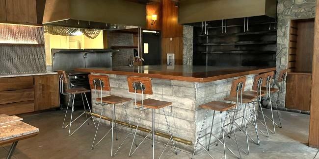 An empty restaurant with a bar with tables and kitchen in the background
