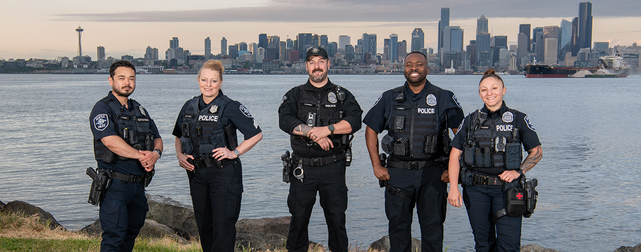 Group of diverse SPD officers standing and smiling with downtown Seattle skyline in background
