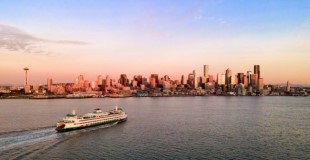 Seattle skyline with orange sunset in background, ferry and water in foreground