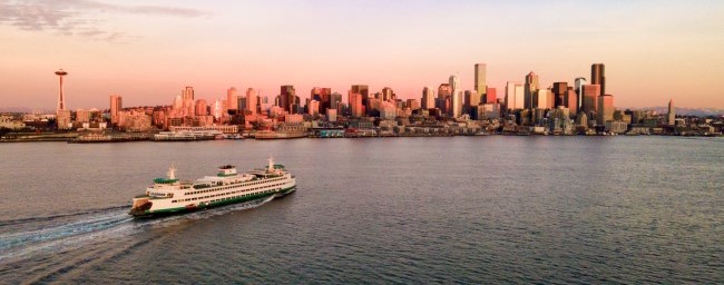 Seattle skyline and orange sunset in background with ferry and water in foreground