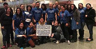 A multiracial group of smiling Seattle staff and volunteers with a sign that reads: SEATTLE UNITED FOR IMMIGRANT AND REFUGEE FAMILIES | SEATTLE UNIDA POR LAS FAMILIAS DE LOS INMIGRANTES Y REFUGIADOS.