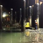 A crew member standing during low tide at night among steel piles